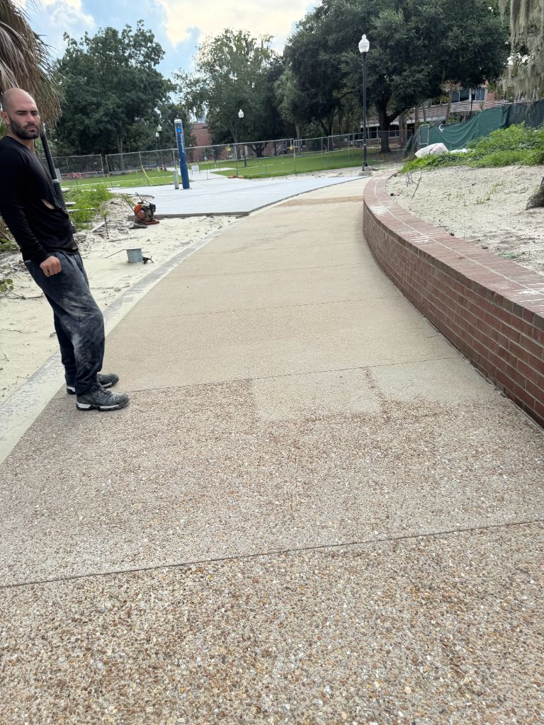 University of Florida campus sidewalk after sandblasting — beautiful exposed aggregate pebble surface revealed, crew member reviewing completed work, matching existing UF campus walkways